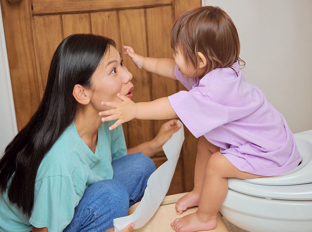 Child reaching for their mama while sitting on the potty